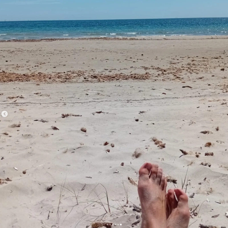 Vista de una playa con pies en la arena y el mar al fondo.