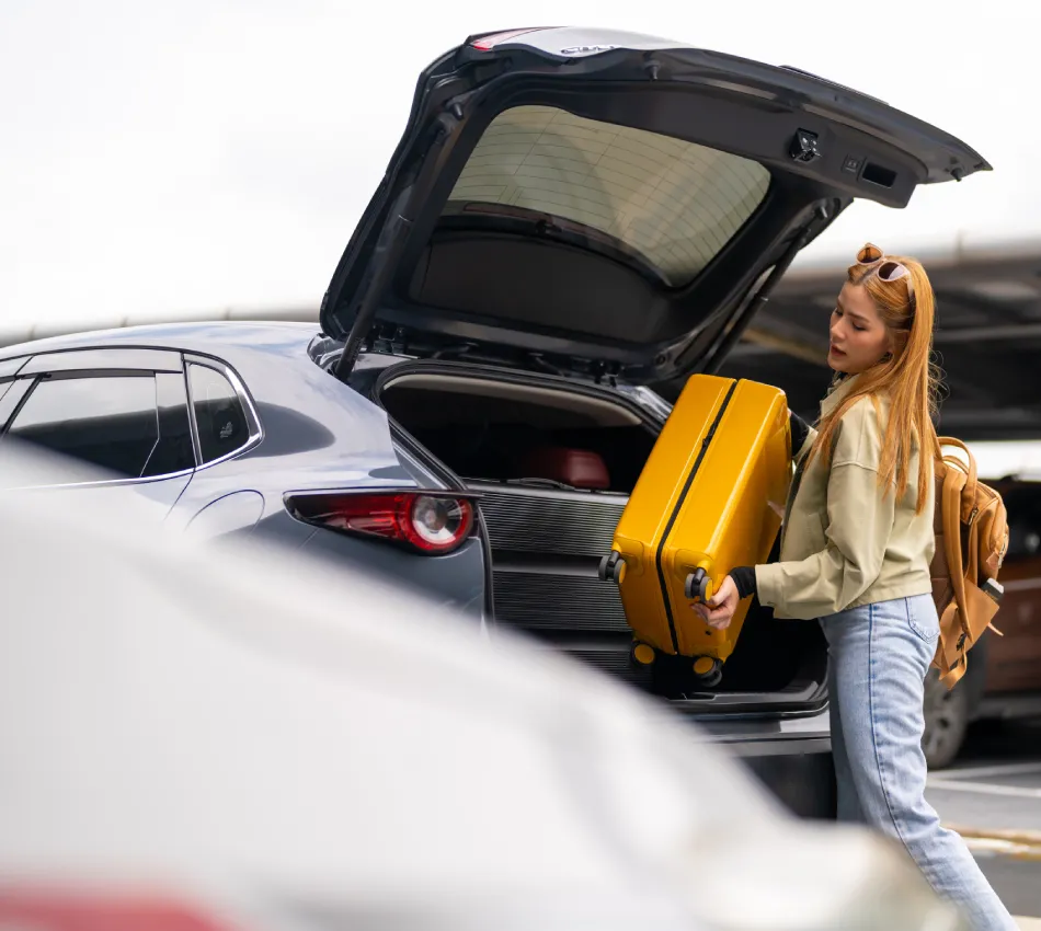 Mujer con maleta amarilla cargando su auto en un estacionamiento.