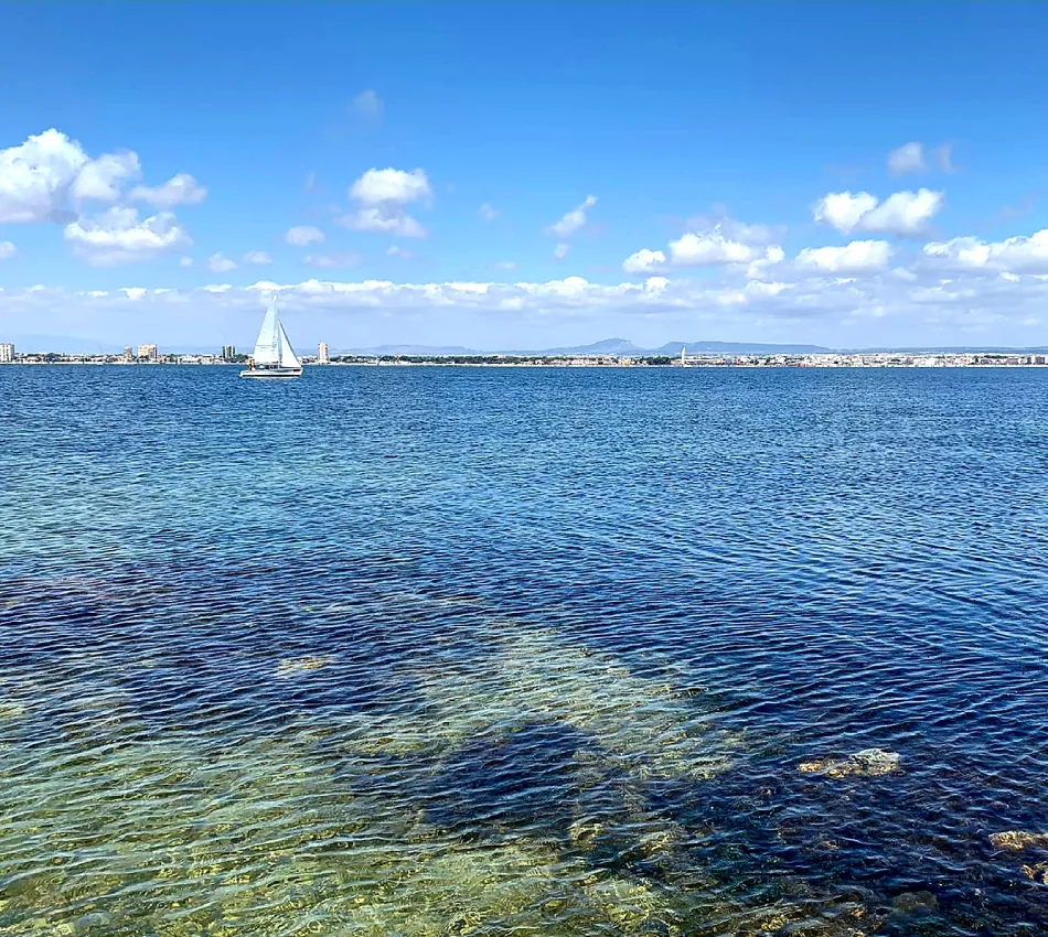 Velero blanco en un mar azul claro bajo un cielo despejado con nubes.