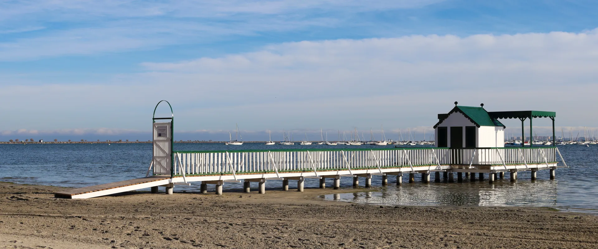 Muelle de madera con caseta y barandilla blanca sobre el mar bajo un cielo azul.