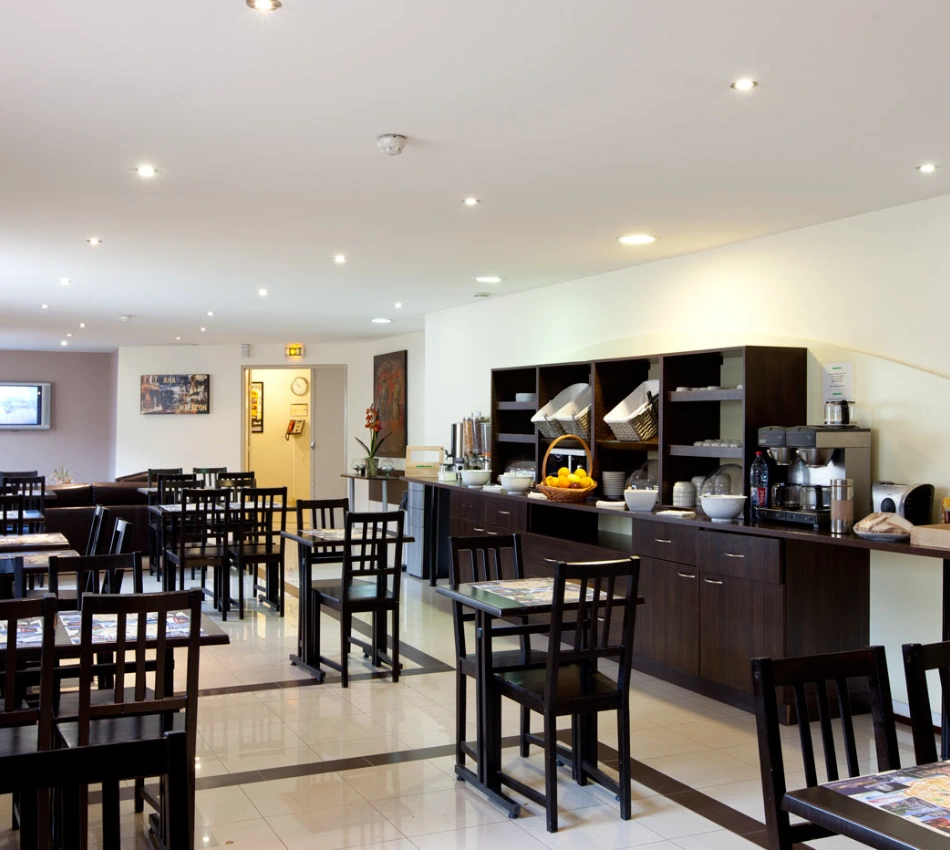 Salle de petit-d&eacute;jeuner moderne avec tables, chaises et buffet.