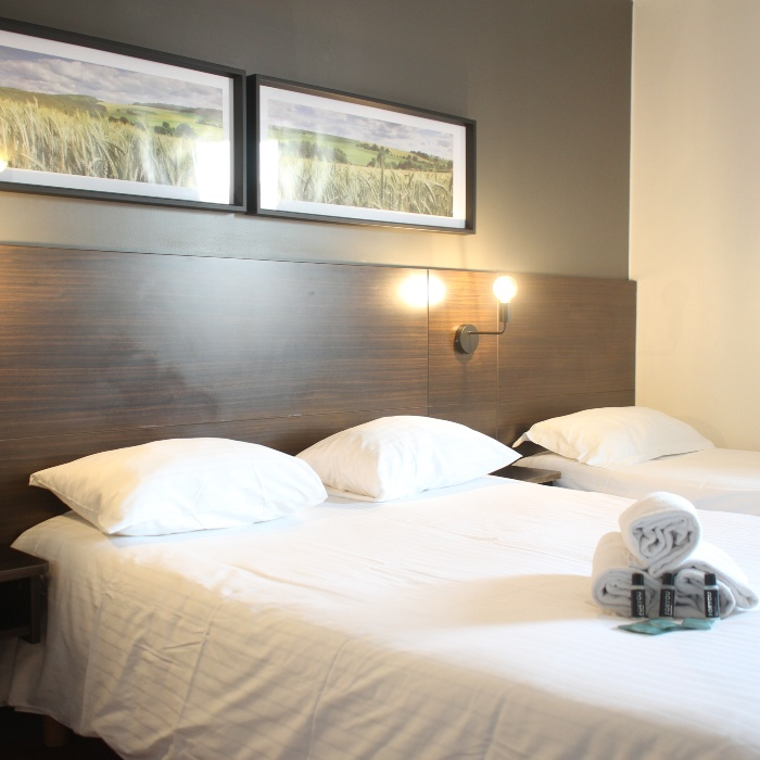 Chambre d'h&ocirc;tel avec deux lits et des cadres au mur.