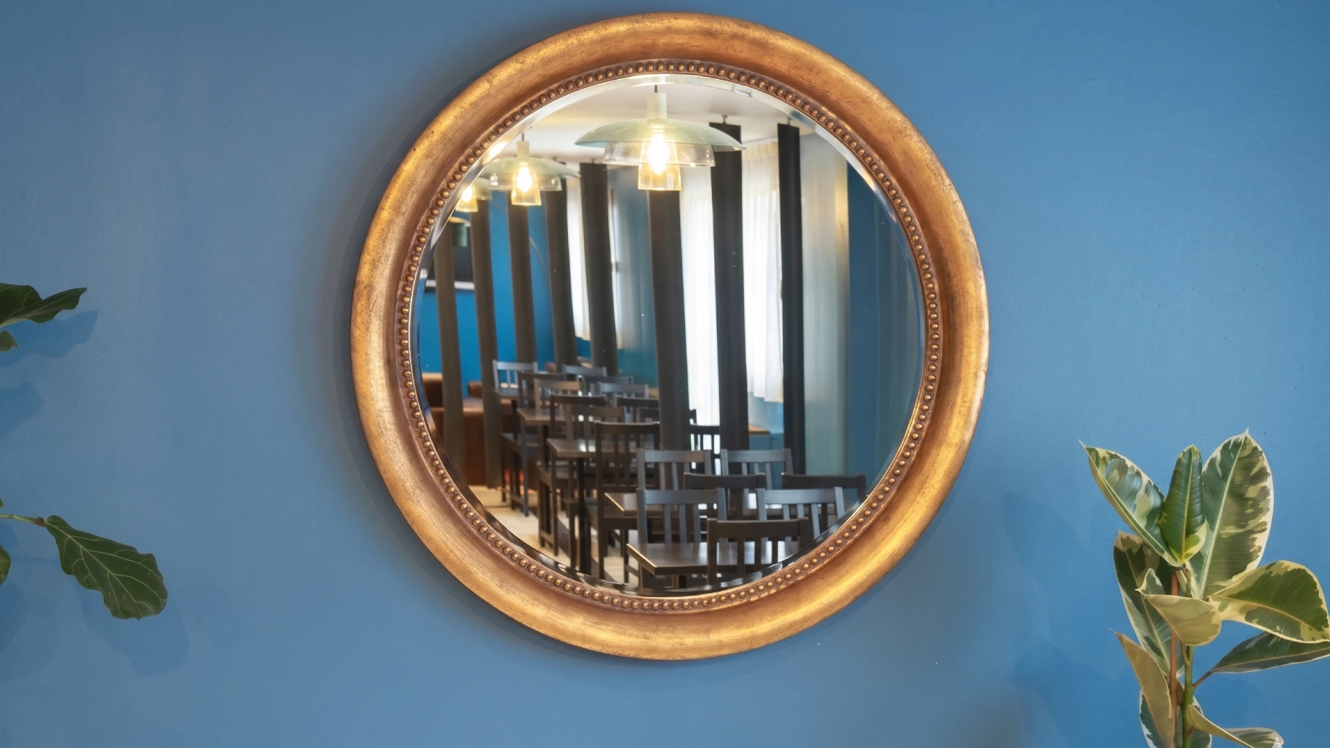 Un miroir rond refl&egrave;te une salle &agrave; manger sur un mur bleu.