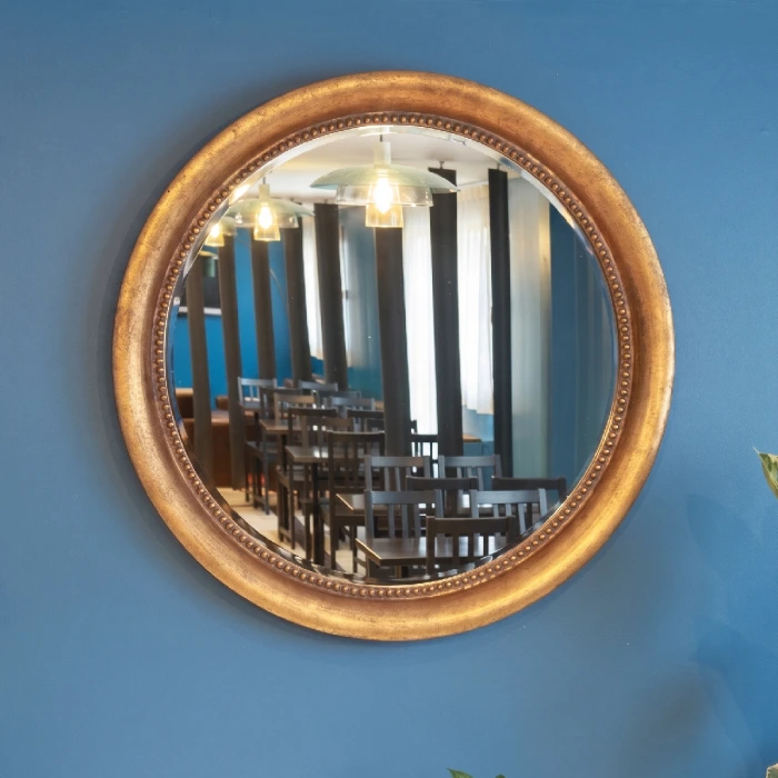 Miroir rond sur un mur bleu refl&eacute;tant des chaises et des tables en bois.