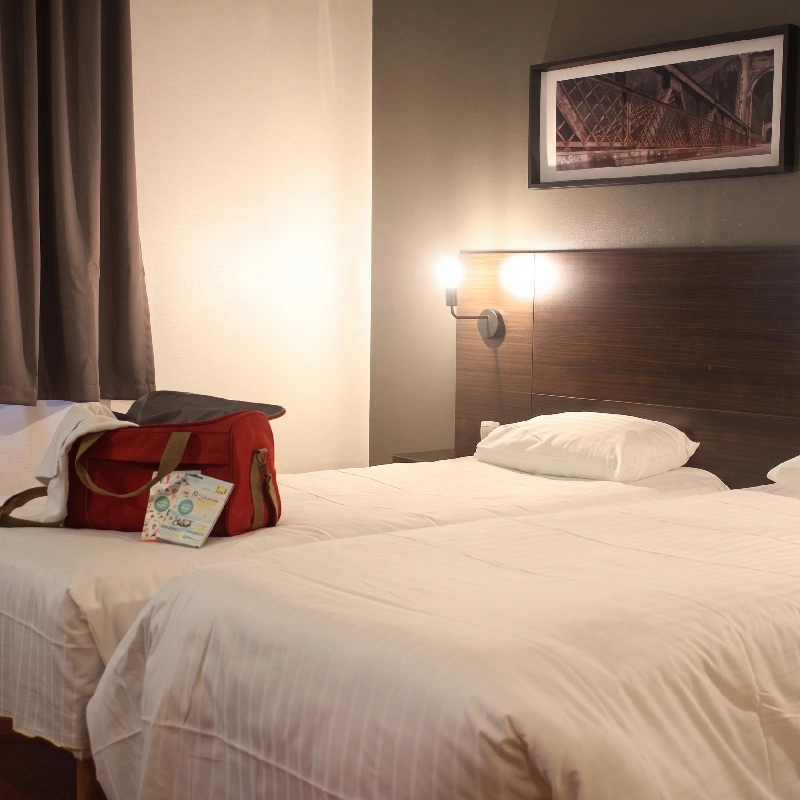 Chambre d&rsquo;h&ocirc;tel avec lit double, sac rouge et tableau mural.