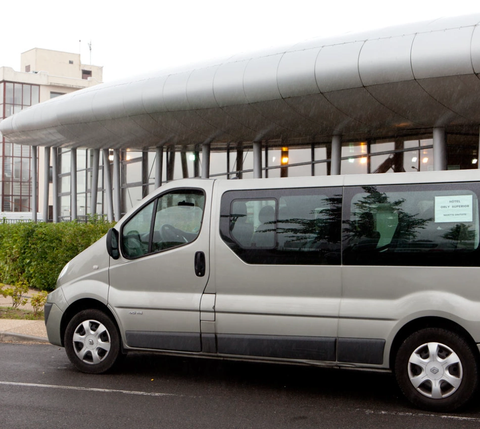 Minibus gris stationn&eacute; devant un b&acirc;timent moderne par temps de pluie.