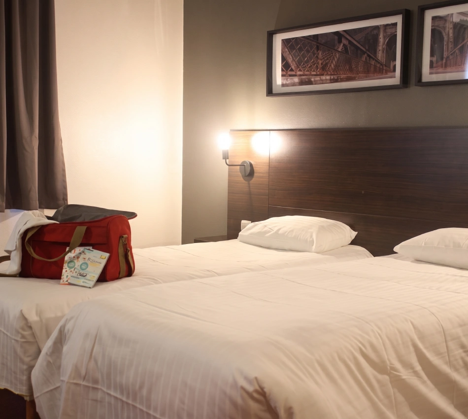 Chambre d'h&ocirc;tel avec deux lits et un sac rouge sur l'un d'eux.