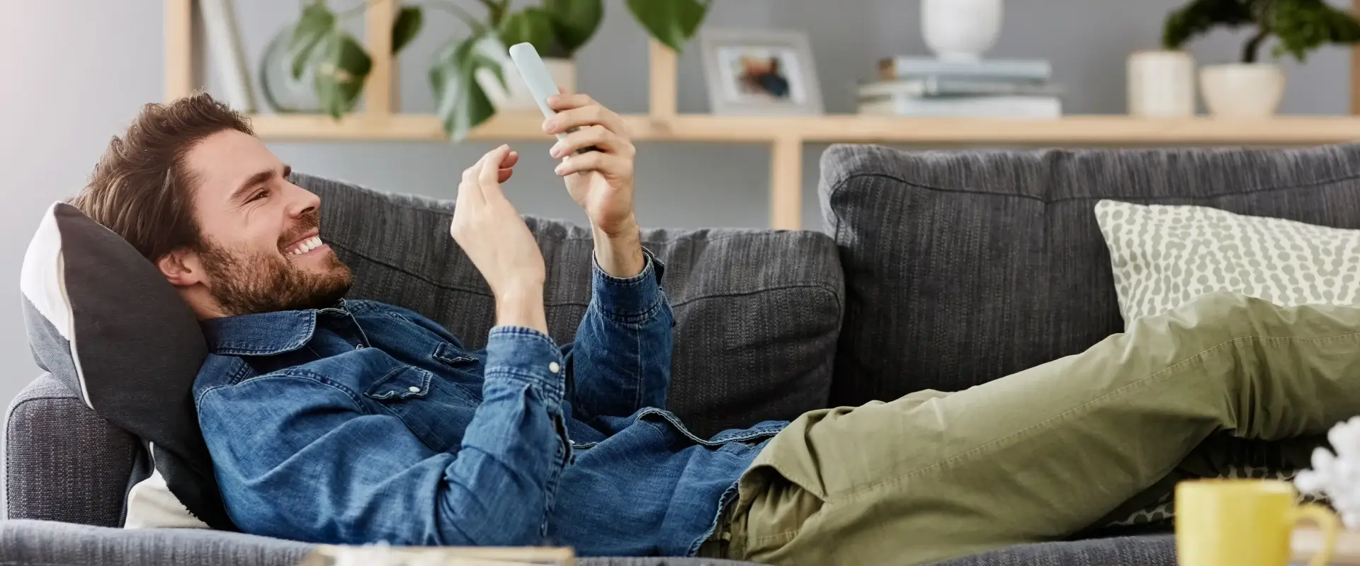 Homme souriant sur un canap&eacute;, tenant un smartphone, ambiance d&eacute;tendue.