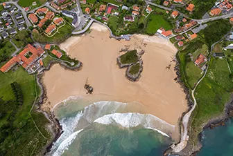 Vista a&eacute;rea de una playa con oleaje, r&iacute;o y edificios costeros.