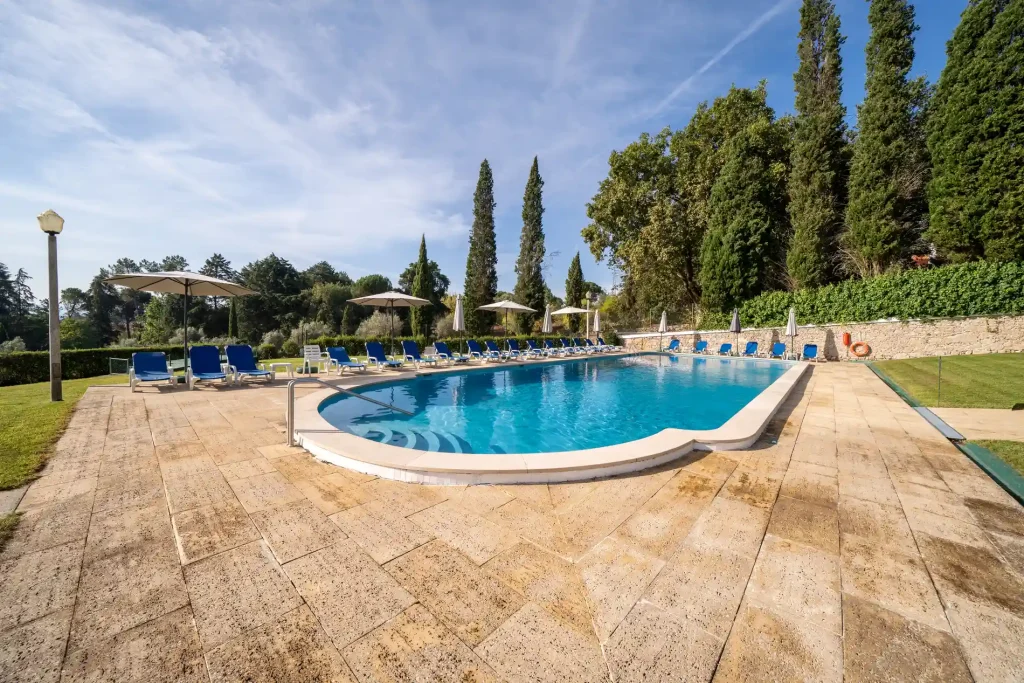 Piscina azul ao ar livre com espregui&ccedil;adeiras e guarda-s&oacute;is no jardim