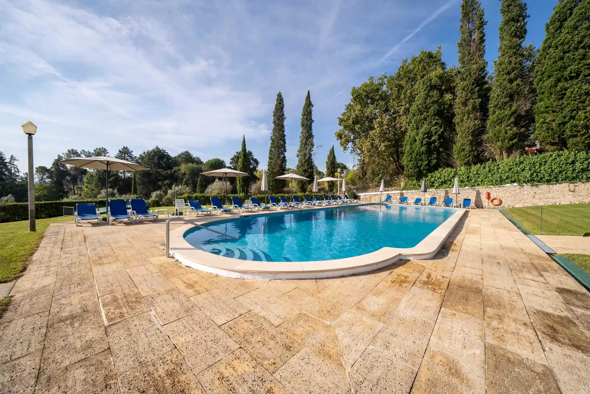 Piscina azul ao ar livre com espregui&ccedil;adeiras e guarda-s&oacute;is no jardim