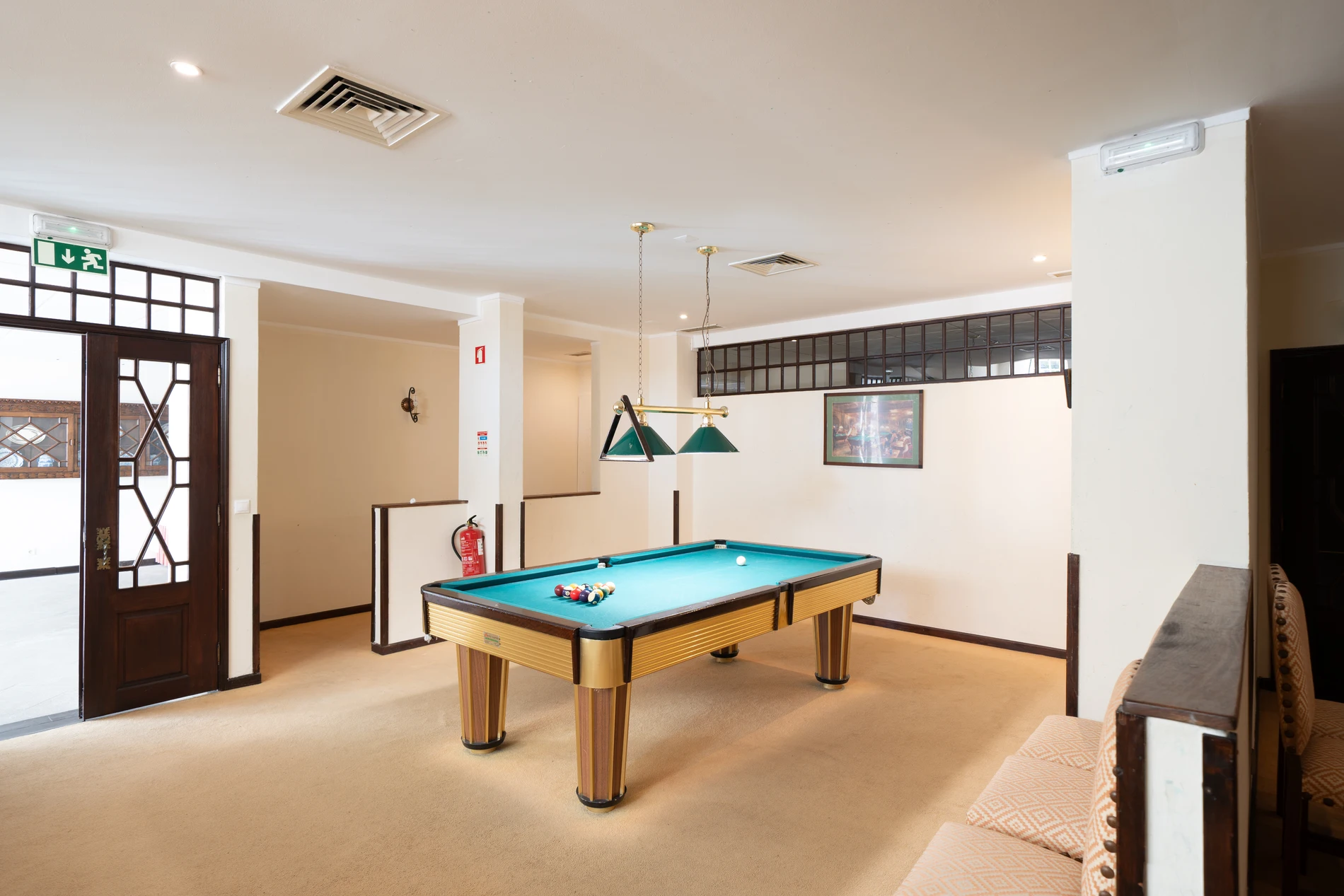 Salão de jogos com mesa de bilhar e luminárias verdes no teto