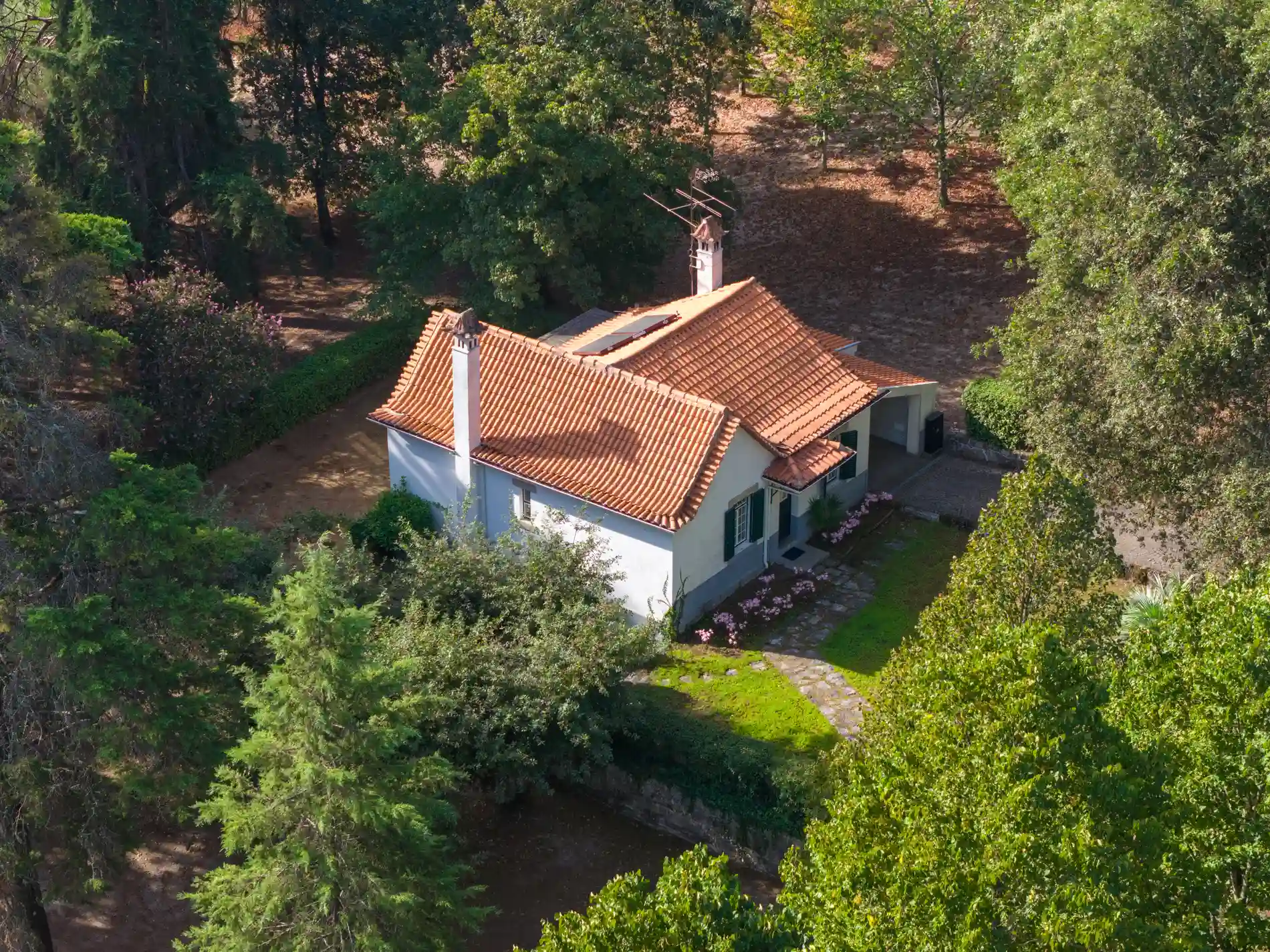 Vista aérea de casa branca com telhado laranja em meio a vegetação verde