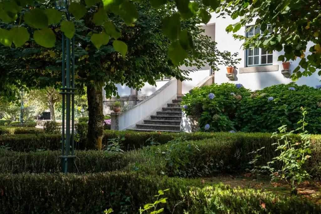 Escadaria de pedra em jardim verde com flores e muro branco ao fundo