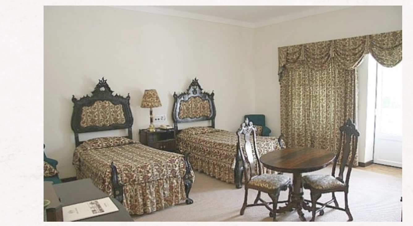 Quarto clássico com camas estofadas, cortinas e mesa de jantar perto da janela