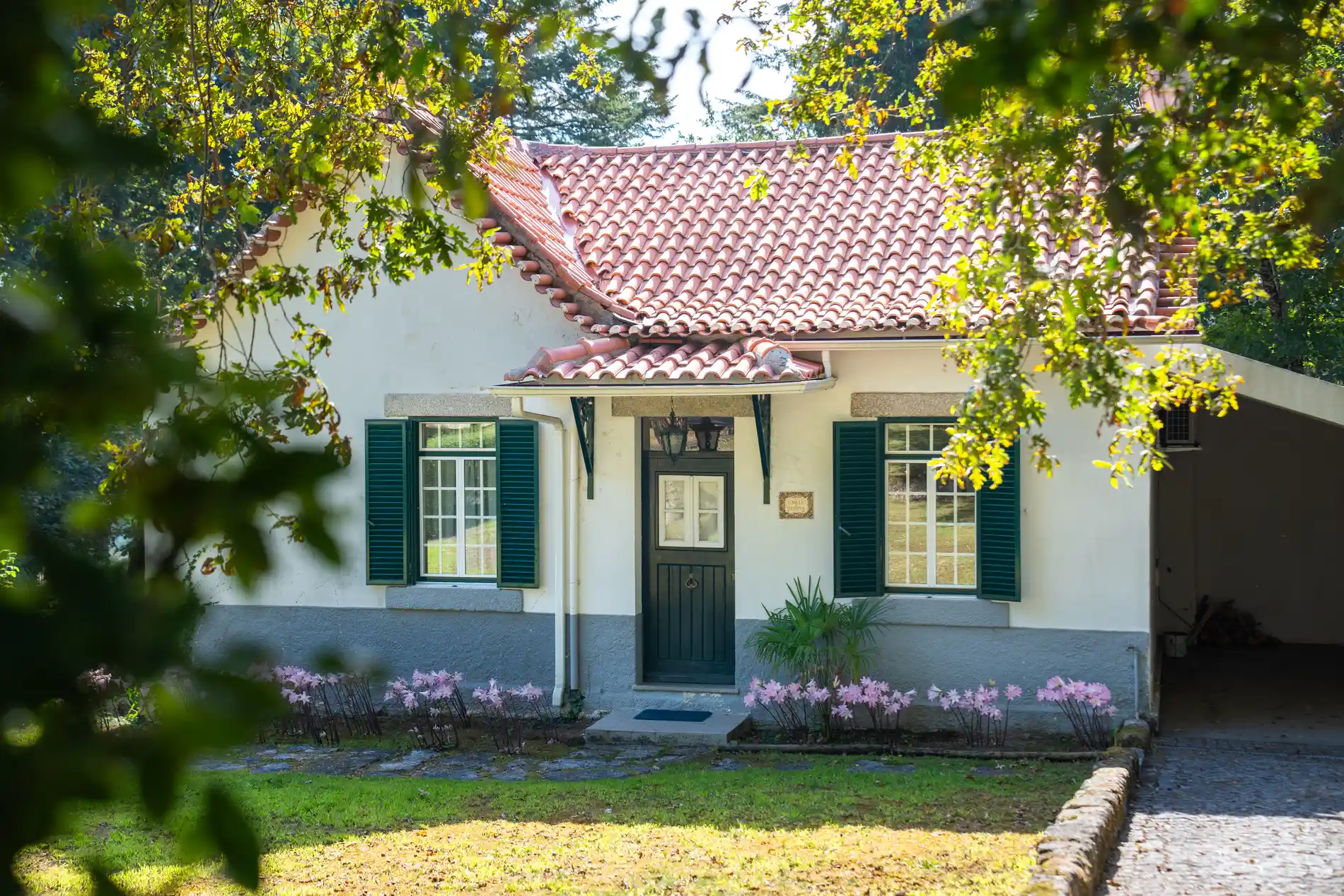 Casa branca com telhado vermelho, cercada por árvores e flores na primavera