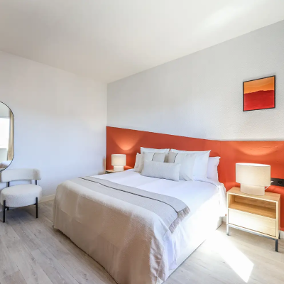 Dormitorio moderno con cama, mesitas y pared naranja.