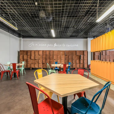 Comedor comunitario con mesas y sillas, paredes de madera y coloridas.