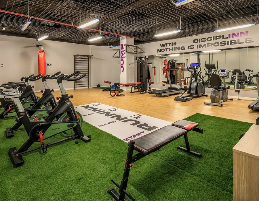 Sala de entrenamiento con m&aacute;quinas, tapete y piso de c&eacute;sped y gimnasio.
