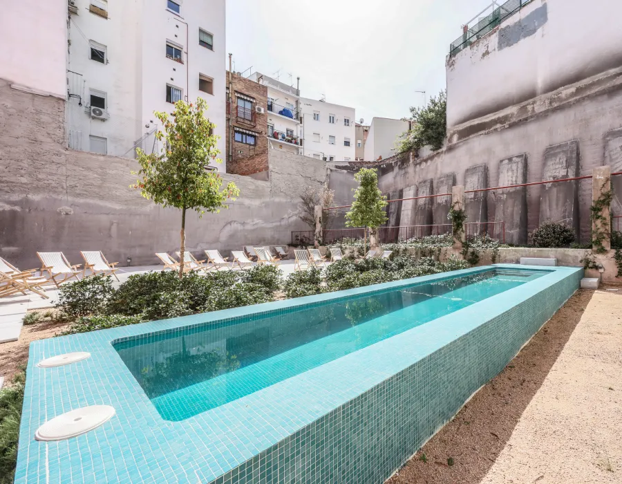 Piscina rectangular turquesa en patio con tumbonas y edificios alrededor
