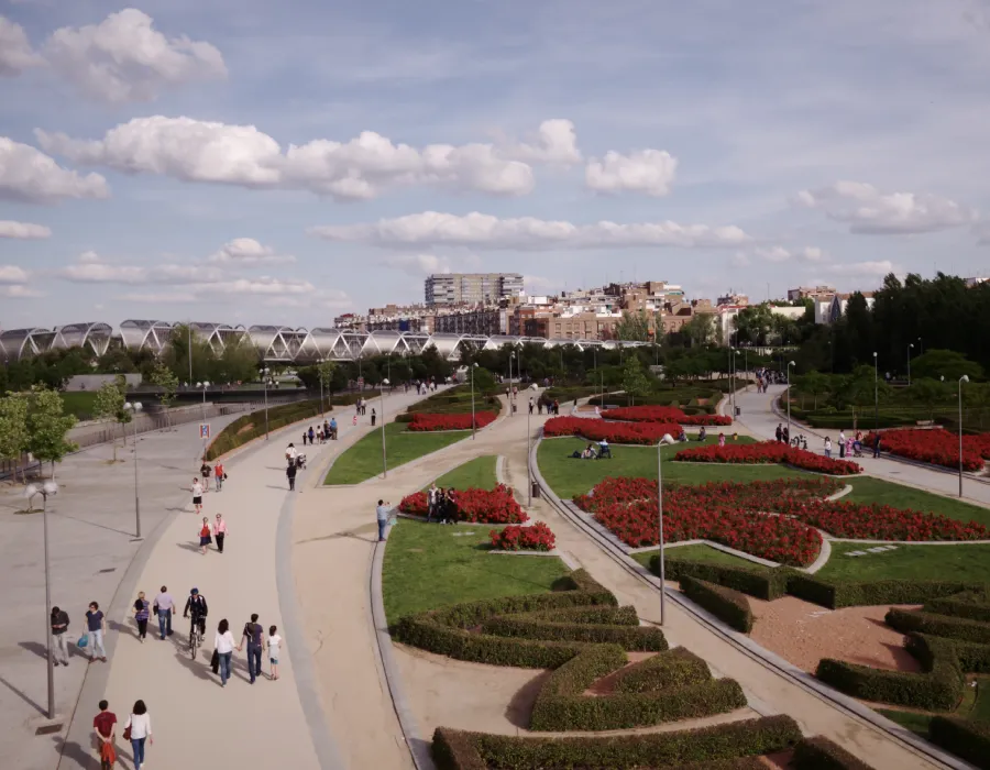 Parque urbano con senderos curvos, flores rojas y vista al r&iacute;o y la ciudad