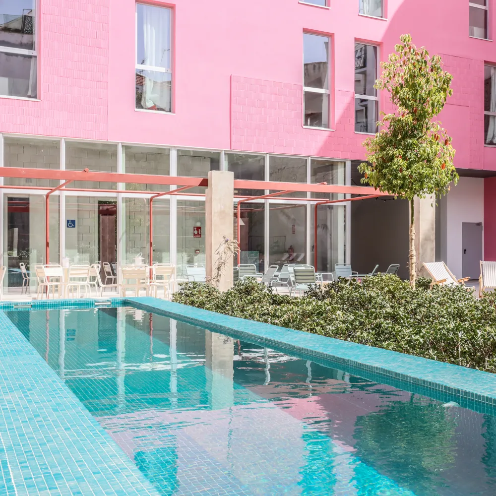 Piscina al aire libre con pared rosa y tumbonas, en patio de hotel