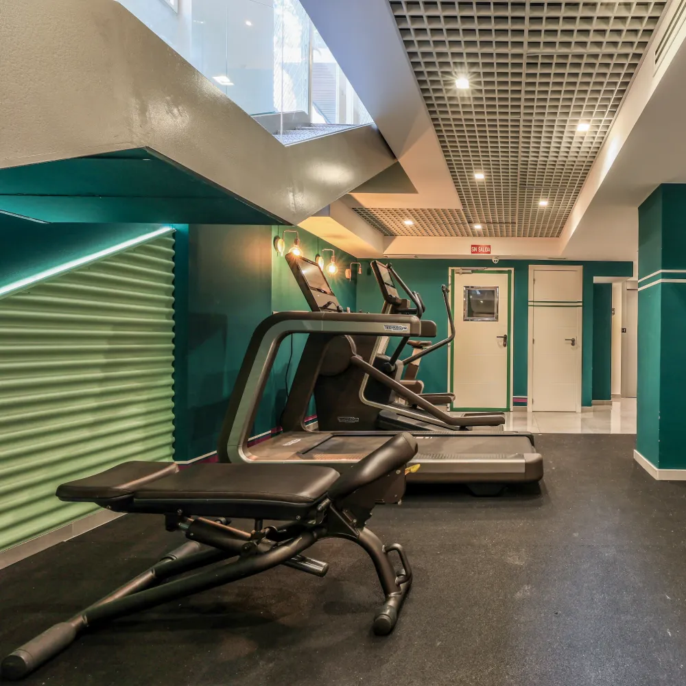 M&aacute;quinas de gimnasio en sala con paredes verdes y techo iluminado