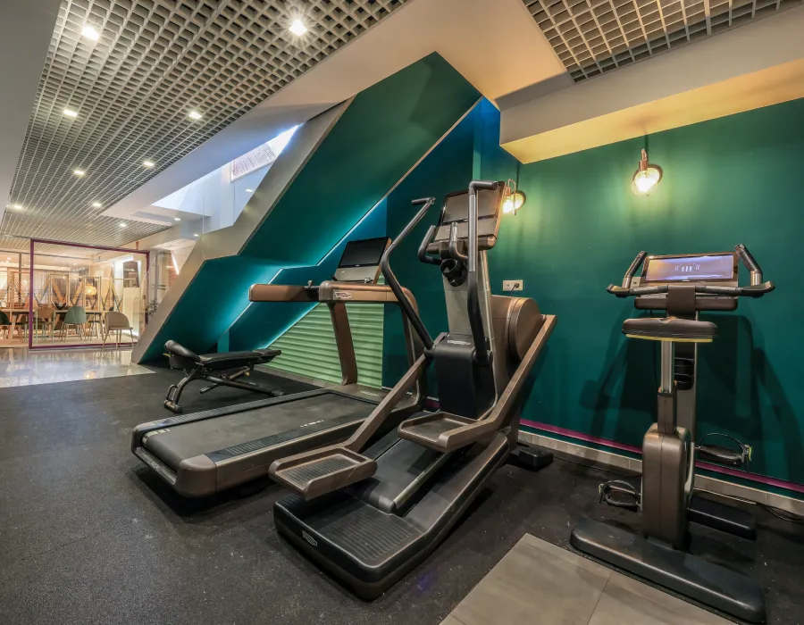 Gimnasio con m&aacute;quinas cardiovasculares y pared verde en interior moderno