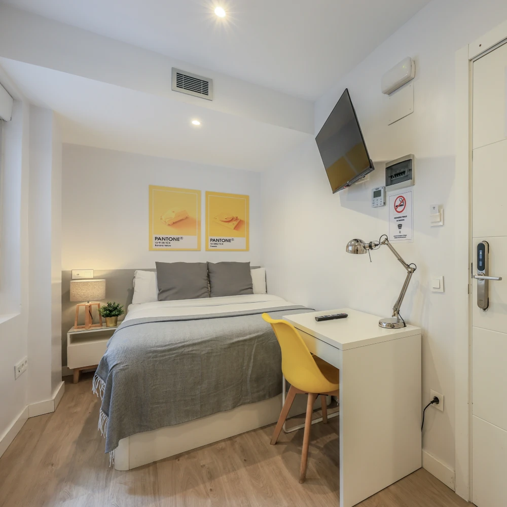 Dormitorio moderno con cama, escritorio amarillo y TV colgada en la pared