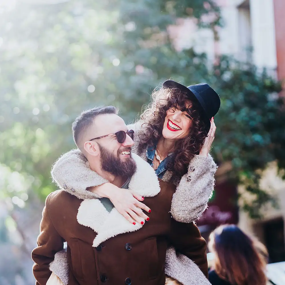 Pareja abraz&aacute;ndose, sonriendo en un d&iacute;a al aire libre, con abrigos de invierno