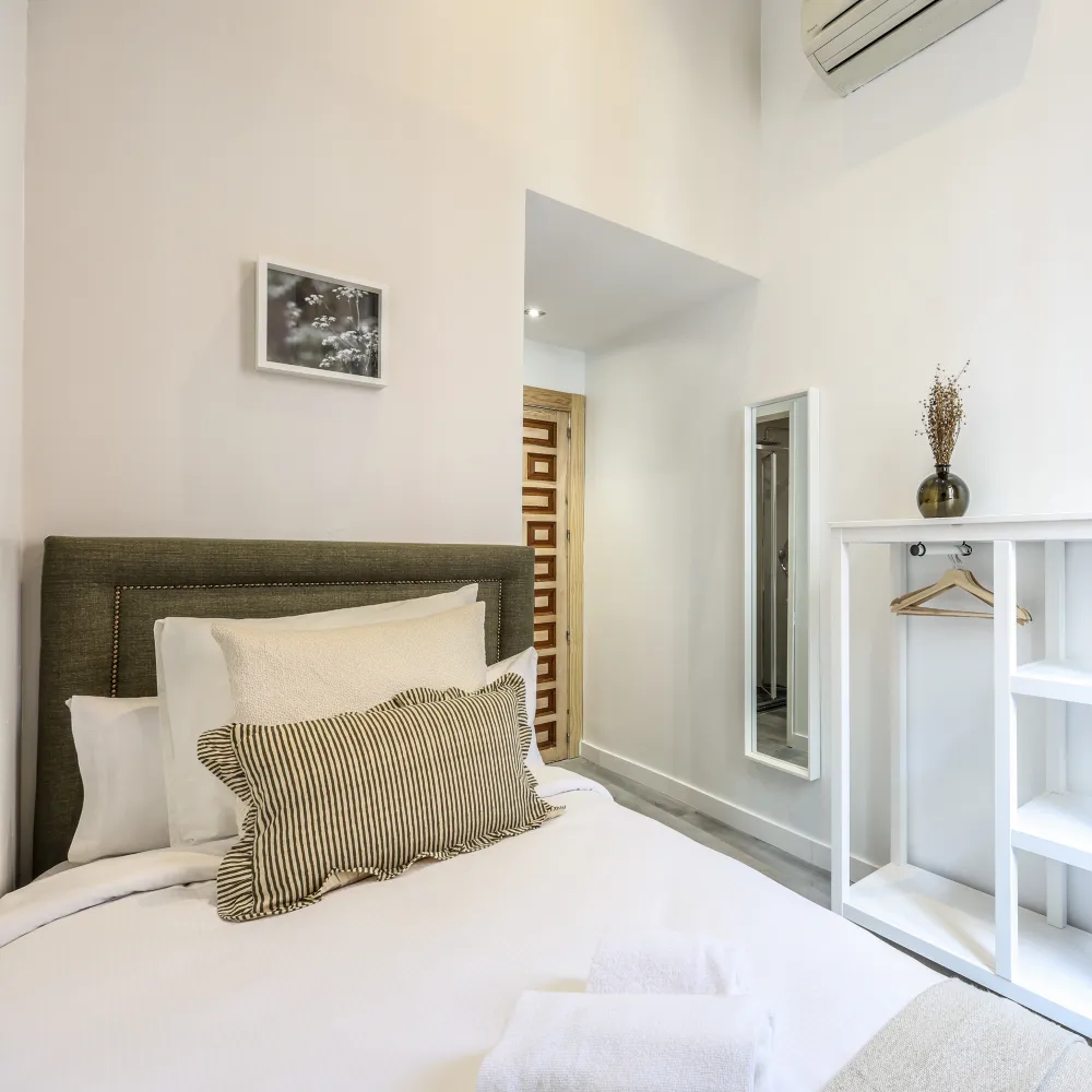 Dormitorio moderno con cama tapizada, cojines y repisa blanca con espejo