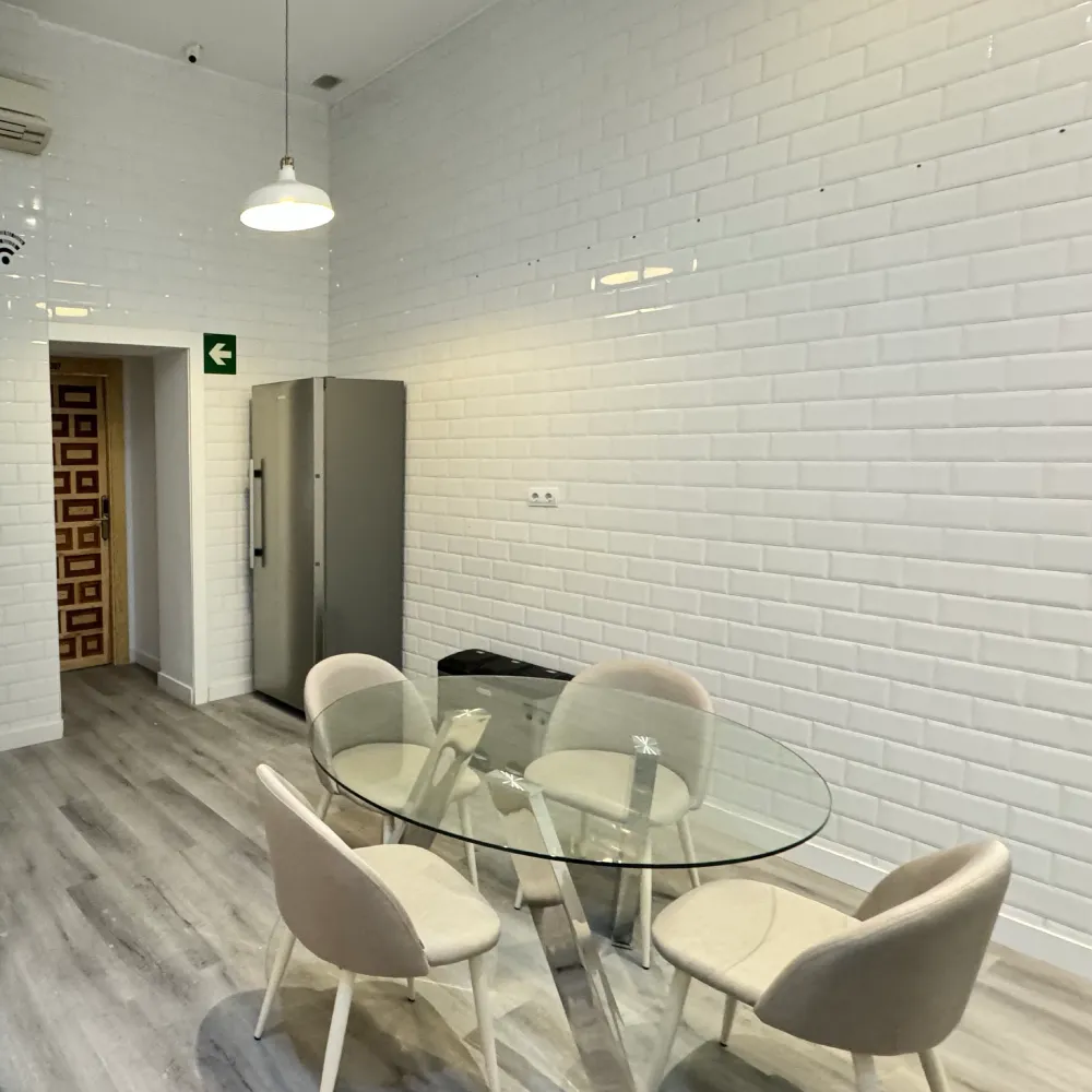 Sala con mesa de vidrio y sillas blancas en pasillo con pared de ladrillo blanco