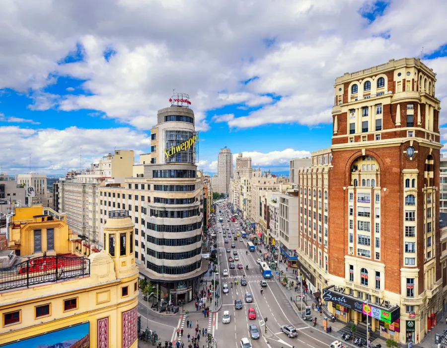 Avenida urbana con edificios hist&oacute;ricos y autos bajo cielo con nubes en Buenos Aires