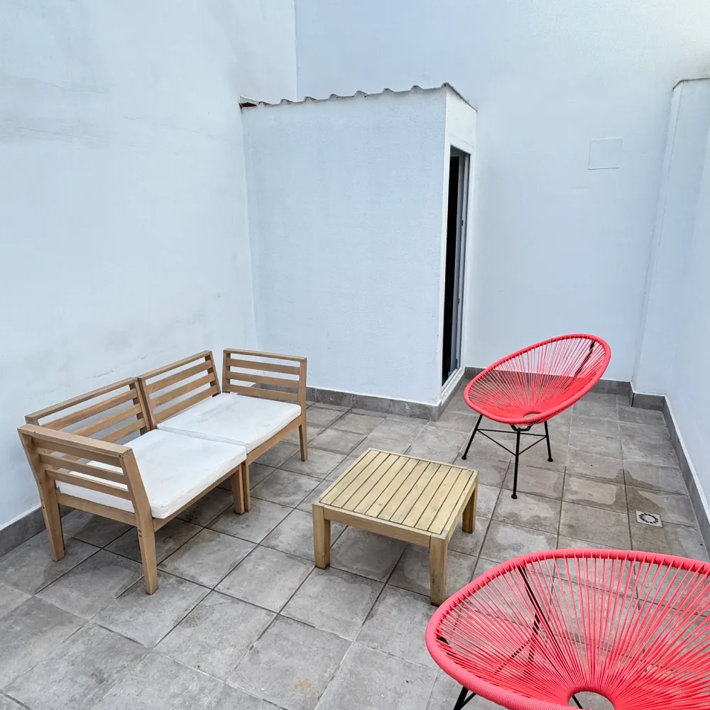 Patio blanco con muebles de madera y sillas rojas en terraza gris