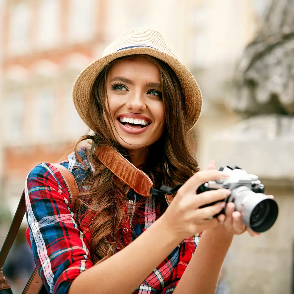 Mujer sonriente con sombrero de paja y c&aacute;mara, al aire libre
