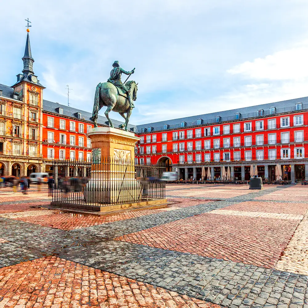 Estatua ecuestre frente a edificios rojos y blancos en una plaza adoquinada