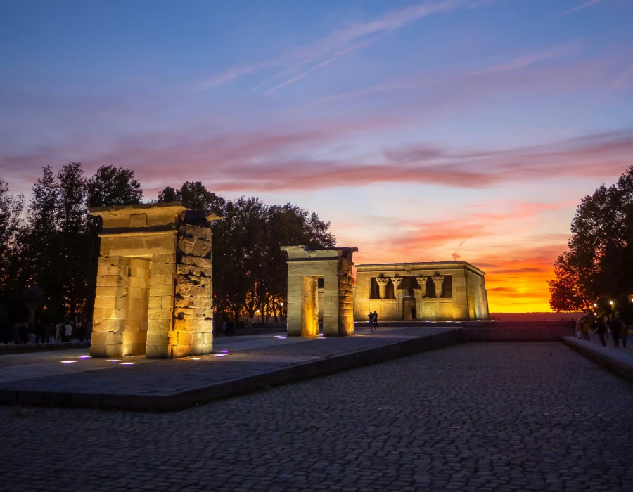 Ruinas iluminadas al atardecer con cielo rojizo y personas paseando