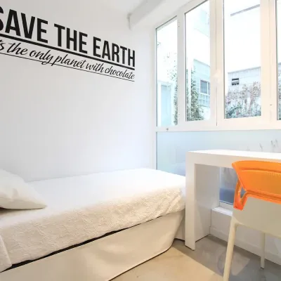 Dormitorio blanco con cama, escritorio y silla naranja, mural &ldquo;Save the Earth&rdquo;