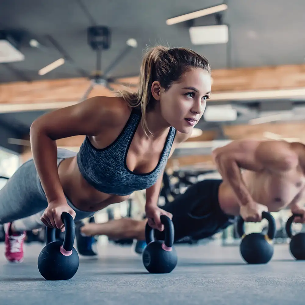 Mujer entrenando en gimnasio con kettlebells en el suelo.