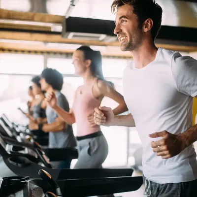 Hombre entrenando en cinta con otras personas en un gimnasio.
