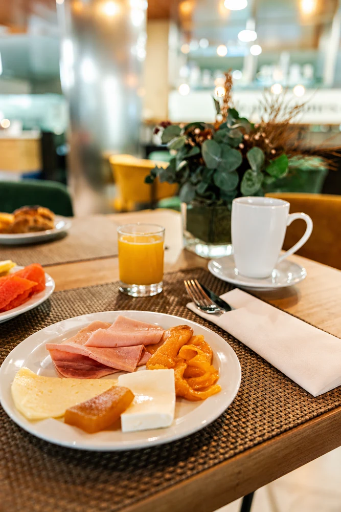 Desayuno en mesa con caf&eacute; en taza blanca y plato con jam&oacute;n y queso