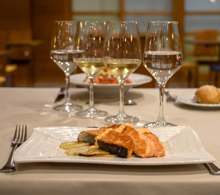 Platos con salm&oacute;n a la plancha y copas de vino en mesa de restaurante.