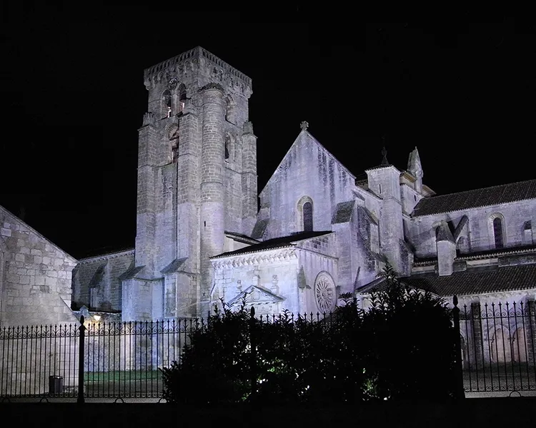 Iglesia de piedra iluminada de noche, torre y fachada con cielo oscuro.
