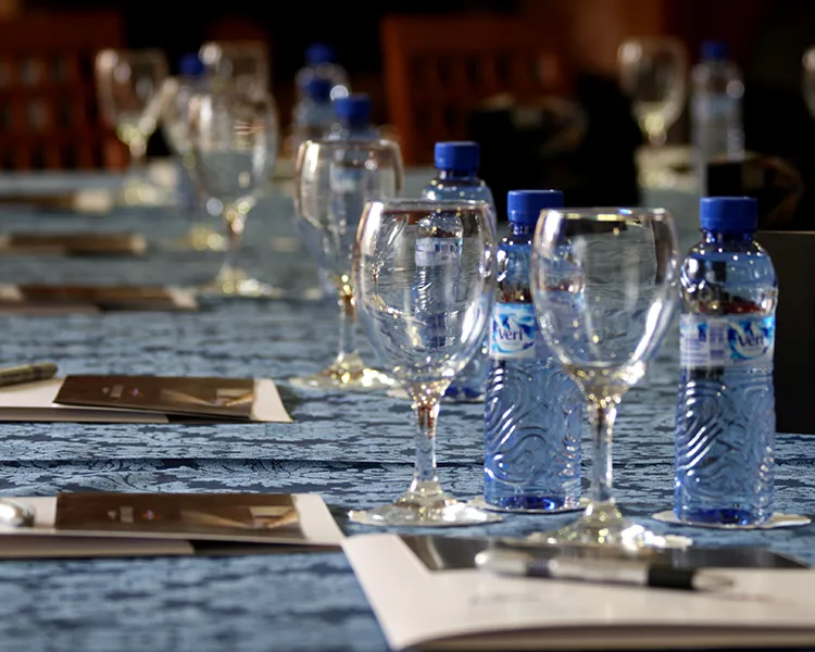 Botellas de agua con tap&oacute;n azul y copas sobre una mesa con mantel.