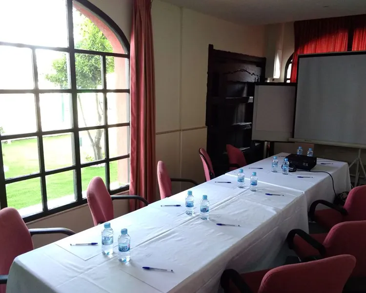 Sala de reuniones con mesas, sillas y botellas de agua junto a ventana.