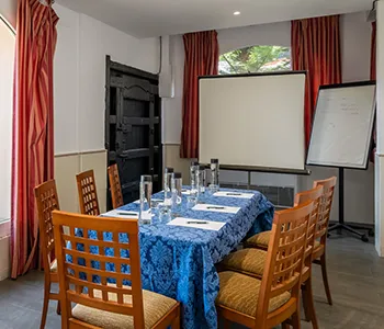 Sala de reuniones con mesa con mantel azul y proyector con pantallas.