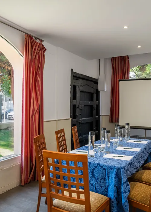 Comedor con mesa puesta, sillas de madera y cortinas rojas.
