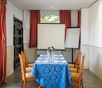 Sala de reuniones con mesa y mantel azul, proyectores y sillas.