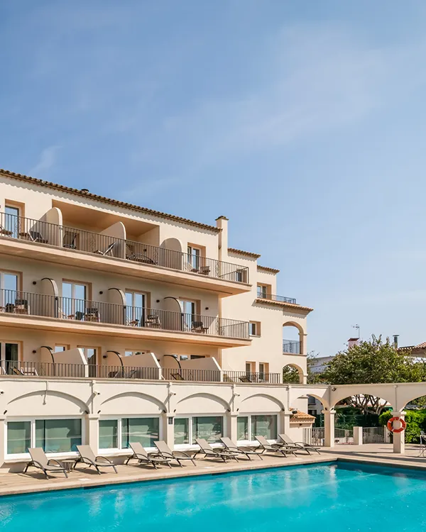 Hotel con balc&oacute;n y arcos, piscina azul al frente bajo cielo despejado