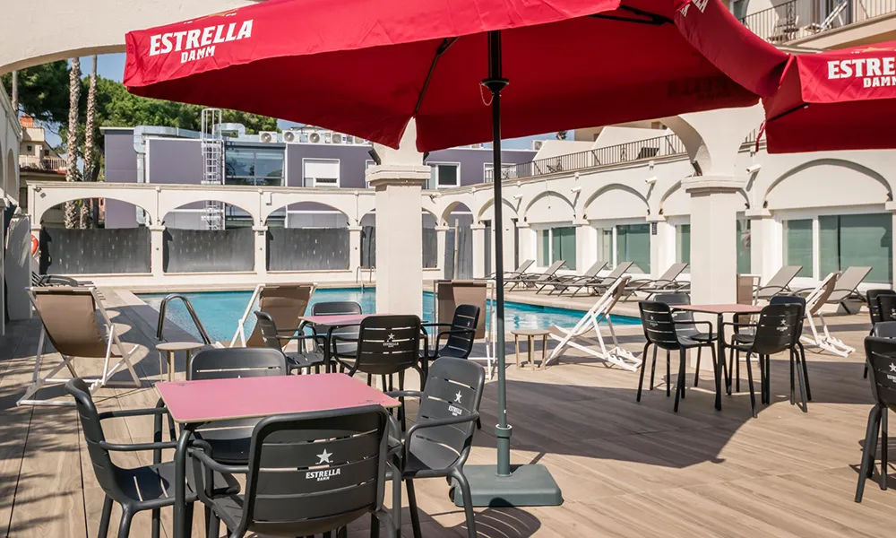 Terraza de hotel con piscina y sillas bajo sombrillas rojas de Estrella Damm.